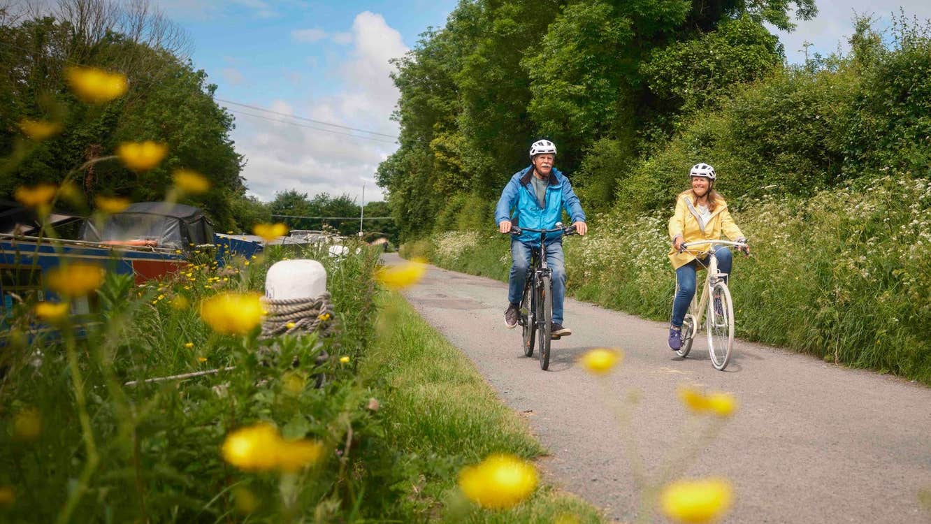 A couple cycling on a route lined with plants and shrubs