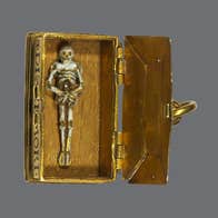 A small, gold coloured ancient box with lid open to reveal a tiny figure of a skeleton lying on the bottom.