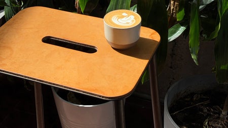 A cup of coffee sitting on a small wooden side table surrounded by indoor plants