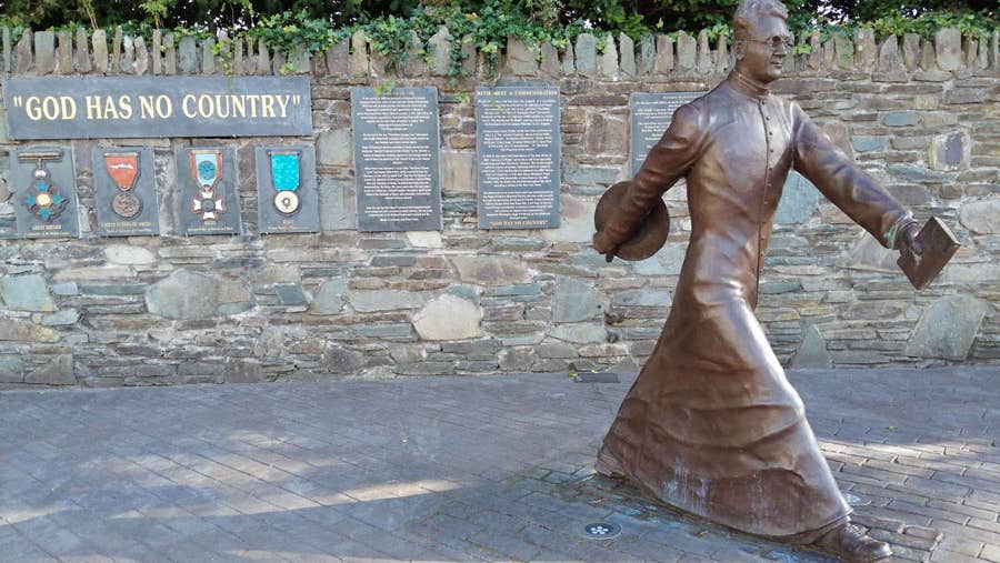 Bronze statue of Monsignor Hugh O'Flaherty captured mid stride with a book in one hand and a hat in the other