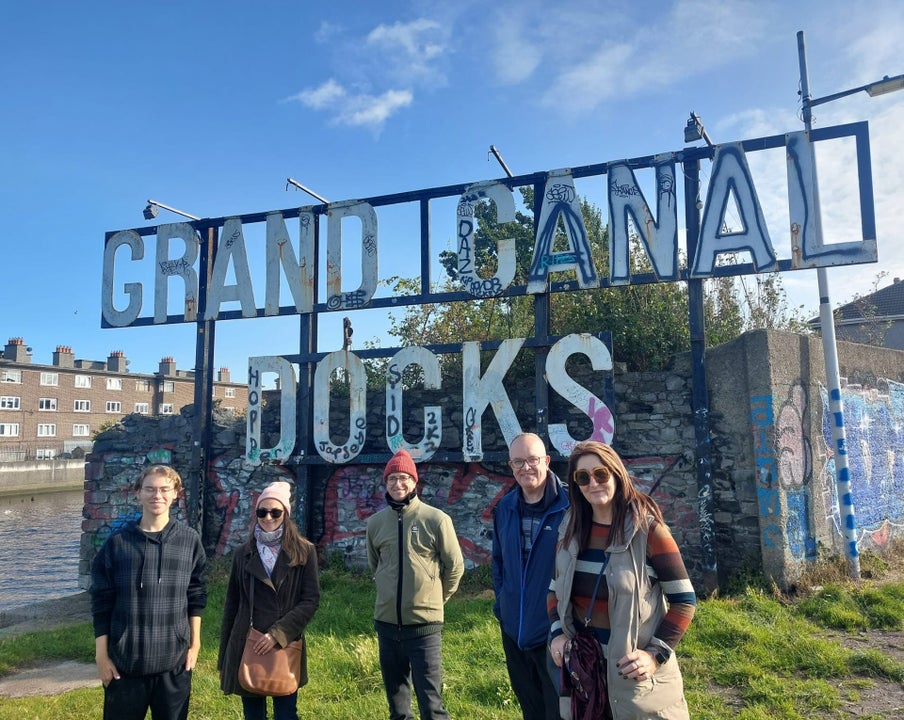 Five people standing on grass in front of a sign that says grand canal docks