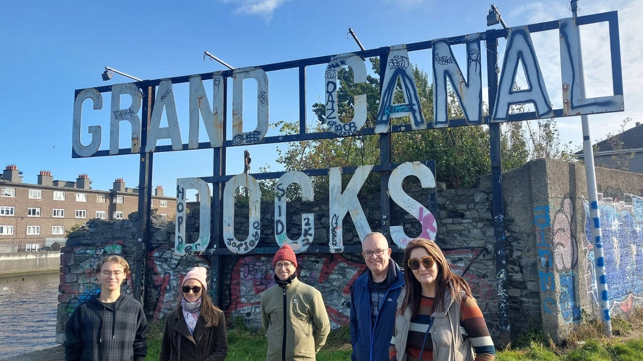 Five people standing on grass in front of a sign that says grand canal docks