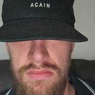 A bearded man with eyes covered by black cap.