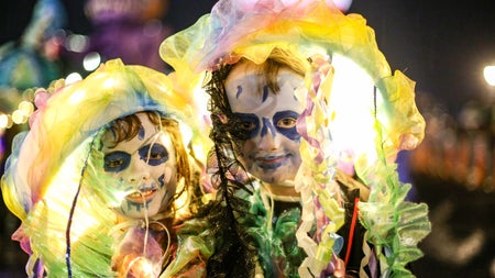Two children in glowing, ethereal costumes with painted skeletal faces take part in Hallowe'en street festival, celebrating Ireland's ancient Samhain roots.