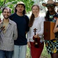 A group of 6 smiling musicians standing under trees