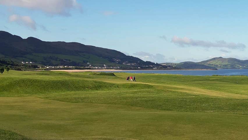 A view of the golf course with two golfers visible in the distance against a backdrop of the headland