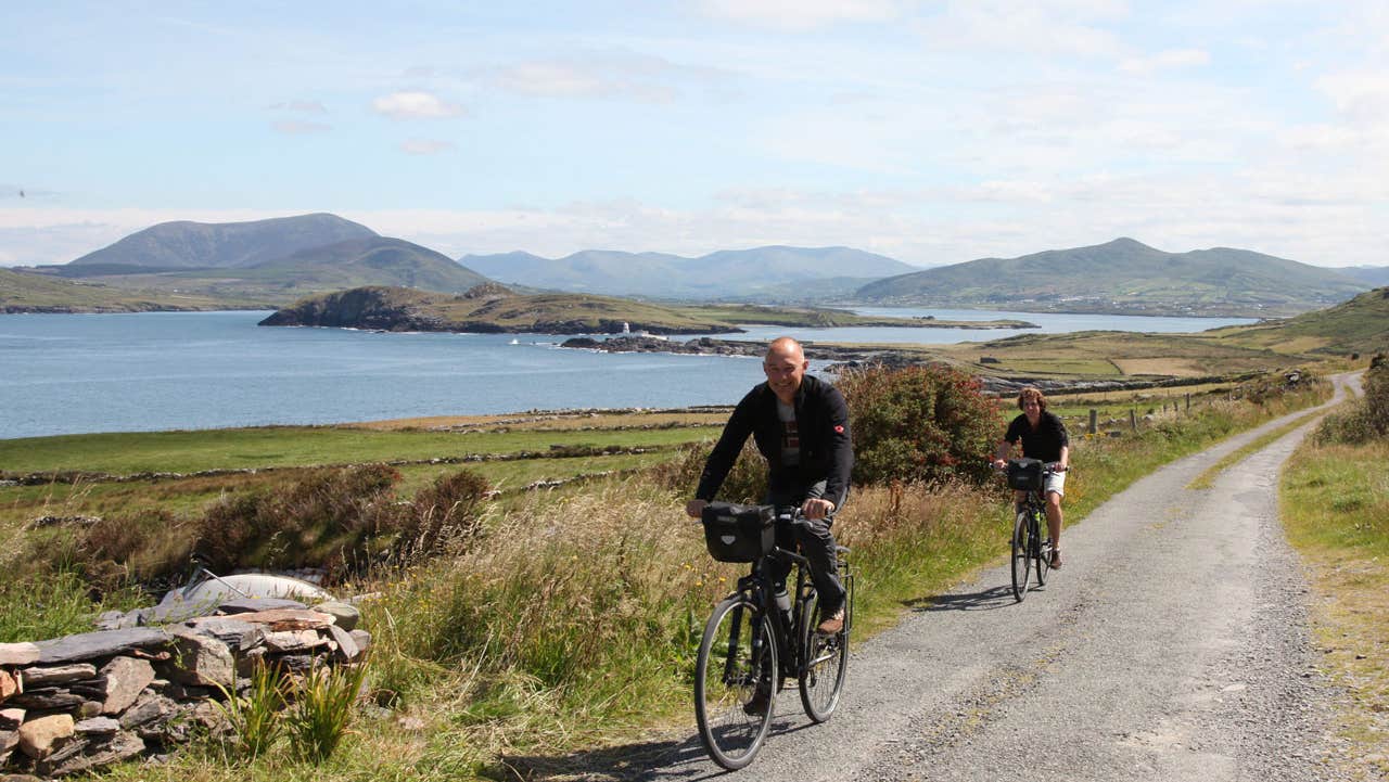 A couple cycling along a quite back road with a sea view in the background