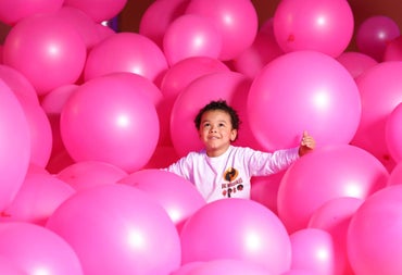 Child looking up while playing among lots of large pink balloons