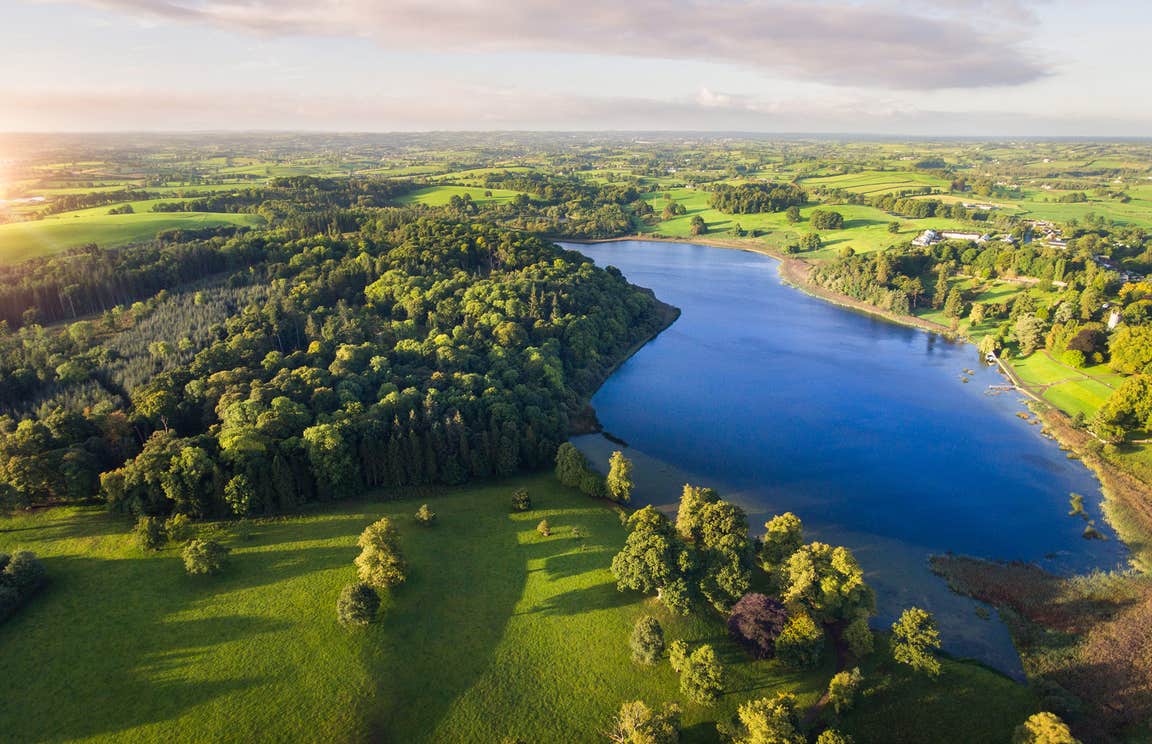 Aerial view of lush green landscapes and a clear blue lake at Castle Leslie Estate