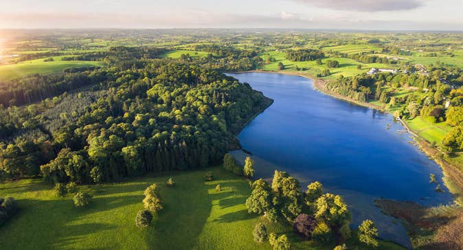 Aerial view of lush green landscapes and a clear blue lake at Castle Leslie Estate