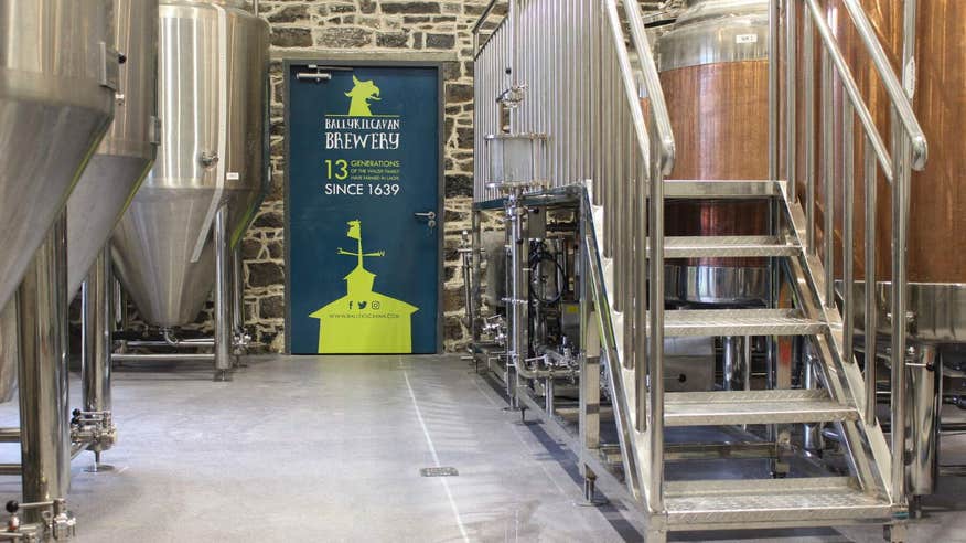 A picture of the inside of the Ballykilcavan Brewing Company with three large vats on the left and a blue door in the centre.