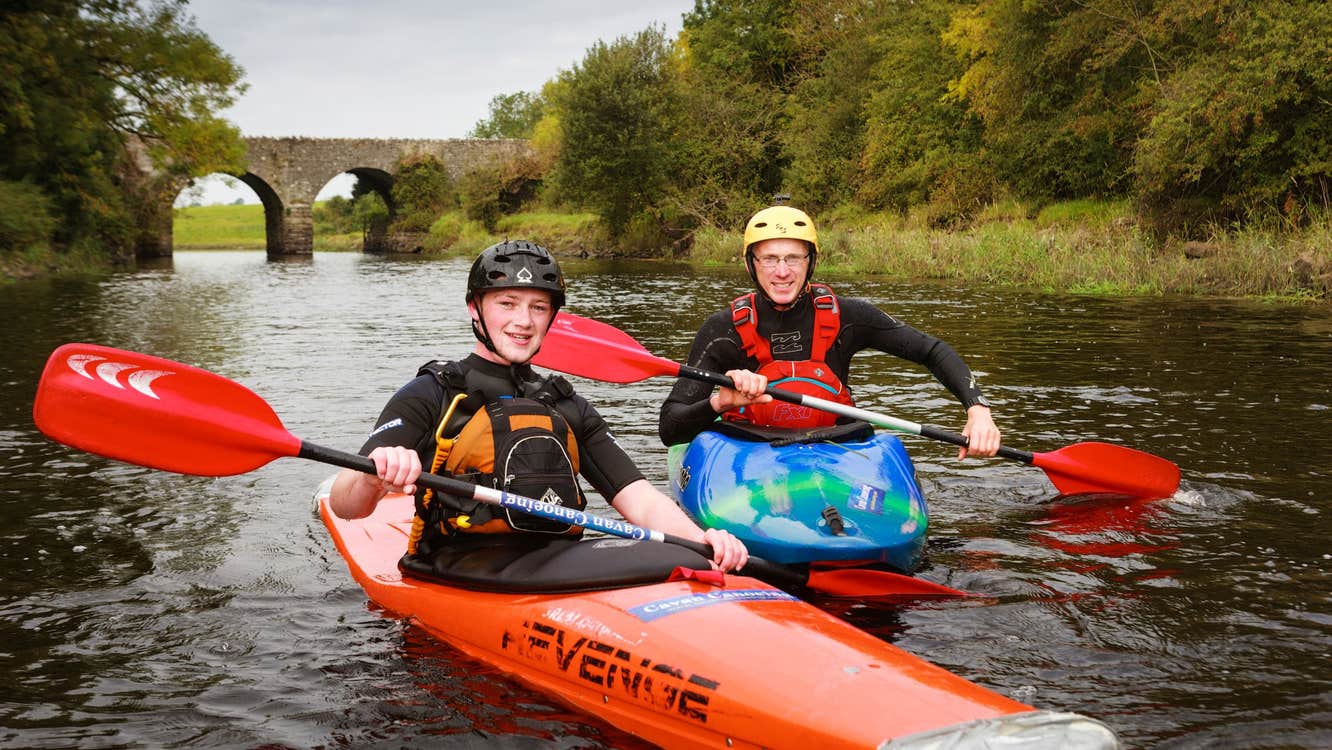 Two people in orange boats kayaking down a river.