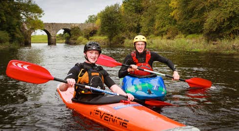 Two people in orange boats kayaking down a river.