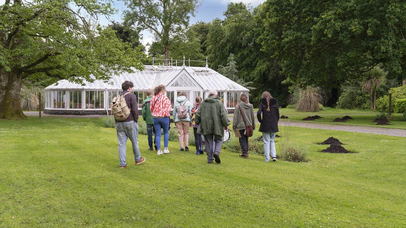 Group of people walking across a lawn to a large, white greenhouse.