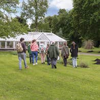 Group of people walking across a lawn to a large, white greenhouse.