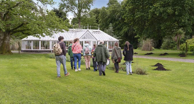 Group of people walking across a lawn to a large, white greenhouse.