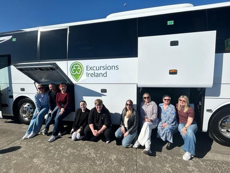 Tour group smiling while sitting by a white tour bus