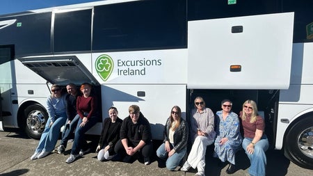 Tour group smiling while sitting by a white tour bus
