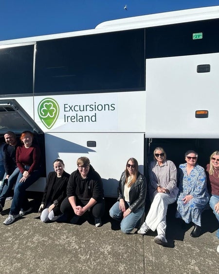 Tour group smiling while sitting by a white tour bus