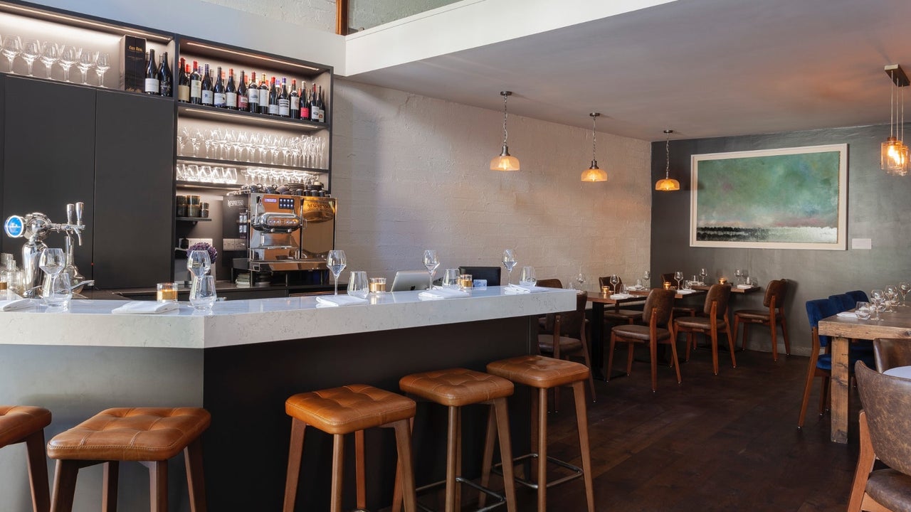Interior of a bar setting with bar stools at the counter and tables set for service
