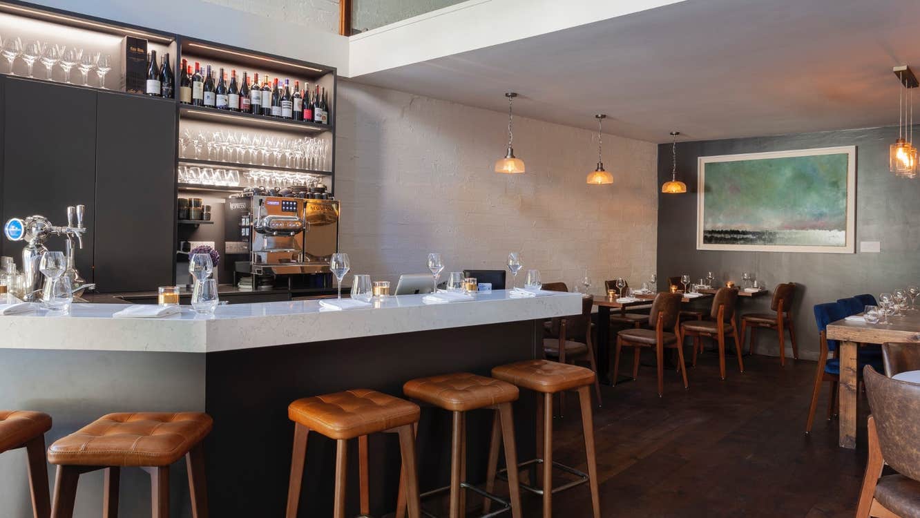 Interior of a bar setting with bar stools at the counter and tables set for service