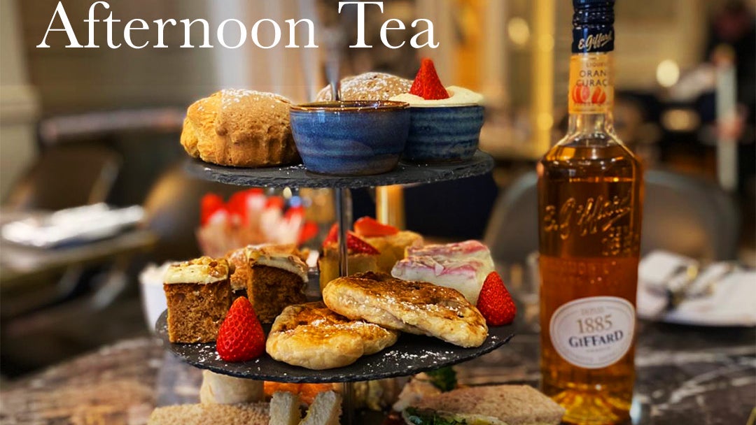 A table with stacked plates full with afternoon tea items including sandwiches, cake, scones