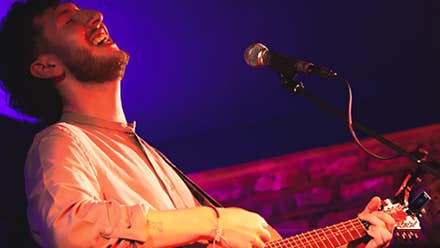 A man singing with head thrown back, playing a guitar.