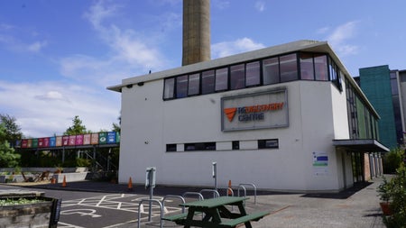 White building with windows on a concrete site with a green picnic bench in front