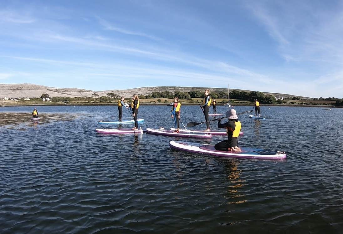 Group in yellow lifejackets on pink paddle boards at sea