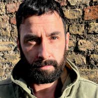 A serious looking man standing in front of a brick wall