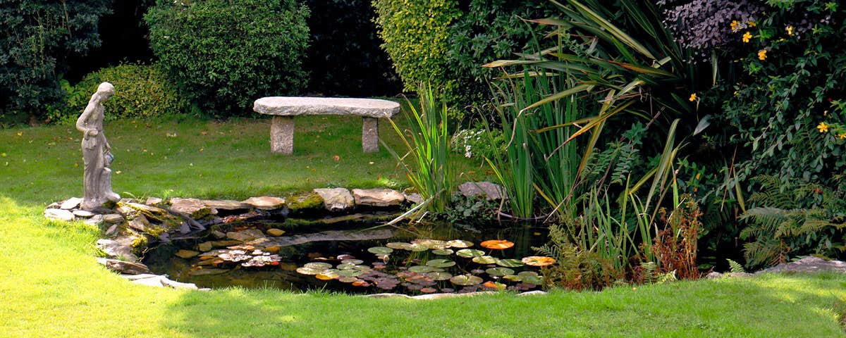 A water pond in the garden with a stone bench and a sculpture at the pond edge