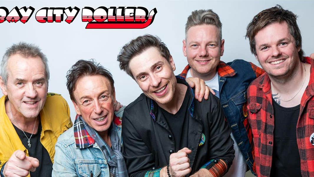 A group of smiling men of various ages, some wearing checked red and black tartan.