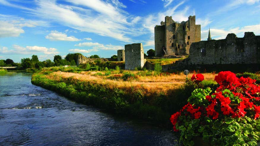 A castle beside a river with vibrant flowers and grass