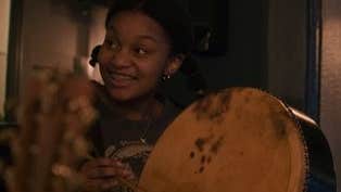 A smiling young woman playing a hand drum.