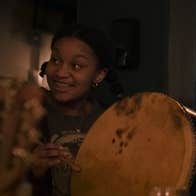 A smiling young woman playing a hand drum.