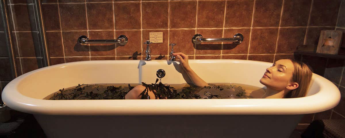 Woman lying in bath with body covered in seaweed