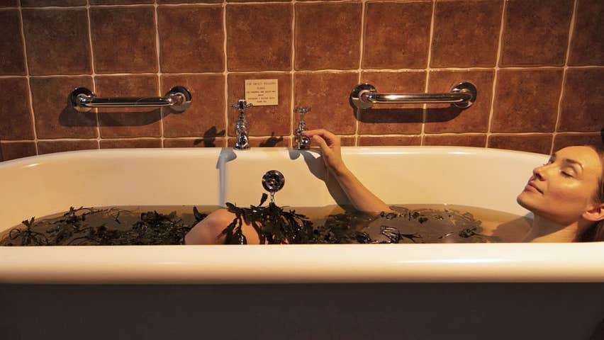 Woman lying in bath with body covered in seaweed