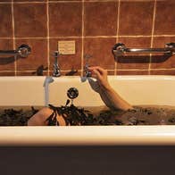 Woman lying in bath with body covered in seaweed