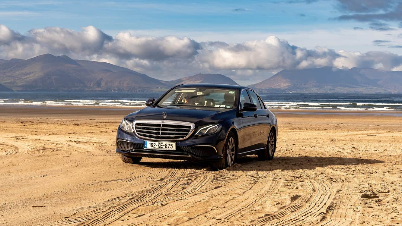 A black Mercedes parked on a sandy beach on a sunny day