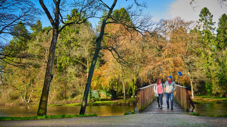 Adult couple crossing a bridge in autumn in Killykeen Forest Park.