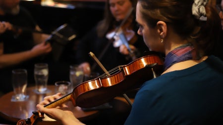 Musicians playing fiddles in a pub with empty glasses on a table