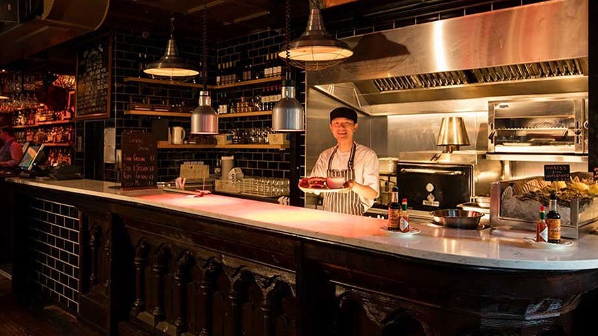 A chef standing at a work station with a plate of food