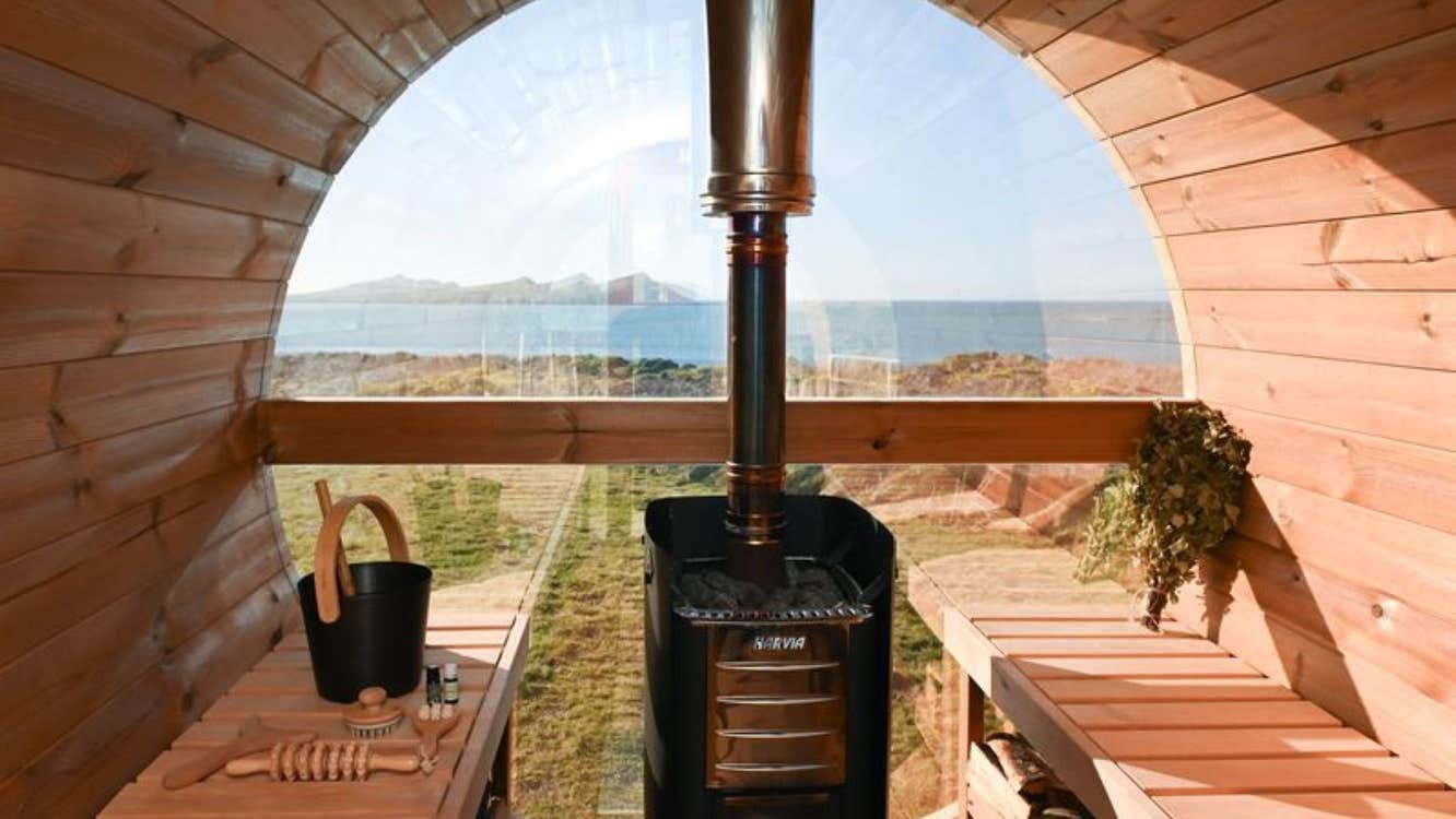 Wood burning barrel sauna interior with bench seating and Atlantic Ocean views through a large window