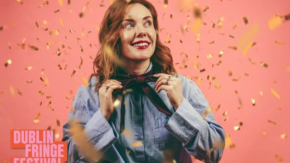 Sadhbh McLoughlin stands in front of a pink background with gold confetti falling around her.