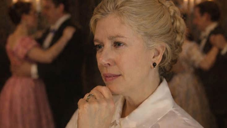 A thoughtful looking woman in white blouse with couples dancing in background lit by candles.