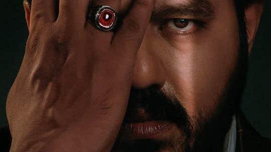 Close up view of a man's face with half covered by his hand wearing a red shiny ring.