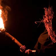 A figure with a straw mask is brandishing a flaming torch.