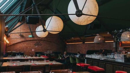 Seating area with exposed brick walls skylights globe pendant lights and a bar with red upholstered seating