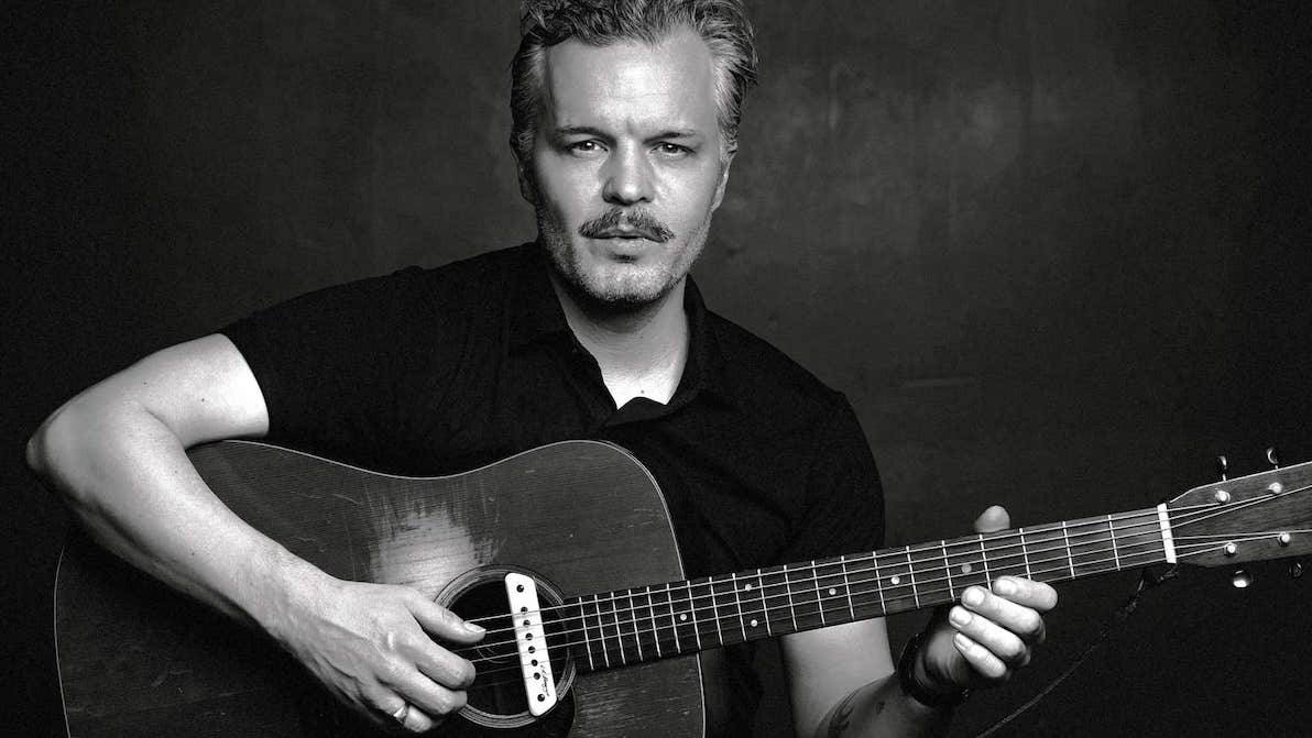 Black and white photo of man playing a guitar against plain dark background