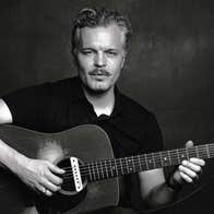 Black and white photo of man playing a guitar against plain dark background